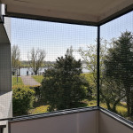 Katzenschutznetz Montage &uuml;ber Balkon-Ecke. Gute Katzensicherung f&uuml;r Wohnung am Fluss oder See. Schutznetz f&uuml;r einen Eckbalkon. Stabiles Katzengitter zum Schutz f&uuml;r Katzen mit Zugang zu Frischluft.